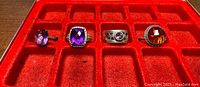 Overview of the four sterling silver rings with different glass stones placed in a red display case.