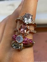 Close-up of four rose gold plated sterling silver rings with visible gemstones on a finger showing size and wear.