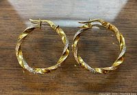 Front view of the pair of twisted 10k gold hoop earrings placed on a wooden surface, showing the circular shape and latch back closure.