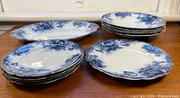 Stacked large oval serving platters and medium-sized plates showing blue floral pattern and scalloped edges.