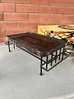 Side angle view of the black cast iron flat top raclette grill on a metal undercarriage stand, showing the flat top and metal framework.