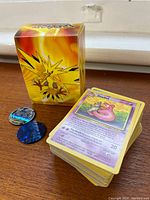 Zapdos deck box, stack of cards, two coins on wood surface