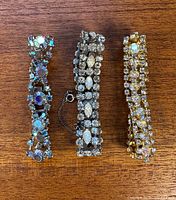 Three vintage rhinestone bracelets laid flat on wooden surface with no visible missing stones.