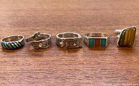 Five vintage sterling silver rings displayed on wood surface showing various designs and stone inlays.