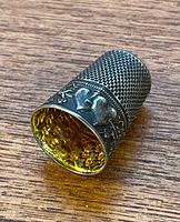 Top and side view of a vintage sterling silver thimble with small dimples for grip and ornate heart design around base, showing age and patina.