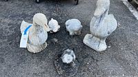 Overview of two large duck statuettes and five frog statuettes of varying sizes arranged on asphalt, showing condition and scale.