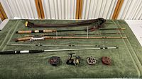Overview photo showing four fishing poles with various handle materials and four fishing reels in front of them laid out on green fabric.