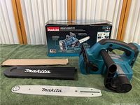 Unassembled chainsaw tool, guide bar, bar cover, packaging, and retail box rest on green surface