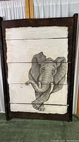 Full view of the elephant artwork on the wooden planks with custom dark wood frame against a white curtain background