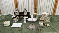 Overview of entire porcelain and mixed figurines and decorations collection displayed on green cloth including busts, deer figurine, clock, dishes, and small decorative items.