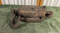 Side view of vintage heavy duty wood hanging pulley showing wooden block, large metal hook and rope groove.