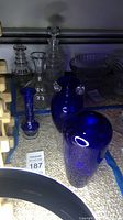 Photo shows three cobalt blue glass vases of different shapes and sizes with other clear glass items in background.