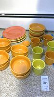 Overview of Fiesta Ware items including stacked coral plates, orange and yellow bowls, mugs, and small dishes all in excellent condition.