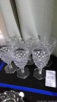 Six clear Fostoria American pattern goblets arranged in two rows on black surface.