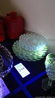 Stack of clear textured Fostoria American pattern glass plates glowing green under UV light