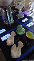 Photo of two white Santini dove glass figurines, green jadeite bird shot glass, purple blown glass candlestick holder, and yellow glass shell item arranged on a surface.