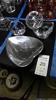 Heart-shaped polished metal dish alongside two clear glass votive holders and a clear crystal rose bowl with etched swirl pattern