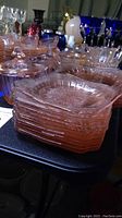 Stack of 14 pink depression glass dinner plates, showing the embossed floral and geometric patterns with a translucent pink color.