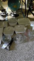 Overview of glassware and casserole dishes arranged on carpeted floor including visible Log Cabin syrup carafe, various Pyrex casserole dishes with lids, multiple glass bowls, and measuring cups.