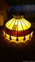 Front angle view of stained glass hanging lamp lit up, showing yellow and brown glass panels and scalloped decorative top.