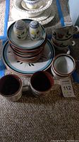 Wide view of stacked plates, salt and pepper shakers, mugs, and matching teacups and saucers showing floral design and colors.