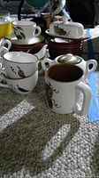 Full lot of Stangl Orchard Song tea set items including teacups, saucers, bowls, creamer, sugar bowl, butter dish, and mug on carpeted floor with natural light.