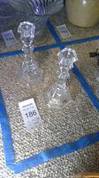 Photo shows two clear, geometric design Tiffany & Co. crystal candlesticks on a beige textured surface with blue tape markings and a MaxSold label for lot 186.