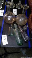 Five vintage glass bottles arranged on a table including two large round-bottom bottles, two rectangular embossed bottles, and one small round bottle.