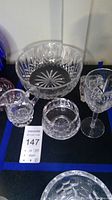 Lot display showing Waterford Lismore crystal glassware: large bowl, creamer, round dish, and wine glass on display with blue vase in background