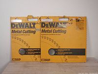 Front view of two yellow Dewalt metal cutting blade packages showing brand, product type, titanium carbide tips, precision teeth, and 14 inch size