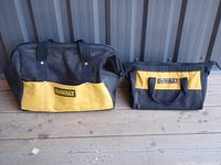 Front view of two Dewalt power tool storage bags, one large and one smaller, both black with yellow front pockets and carrying handles.