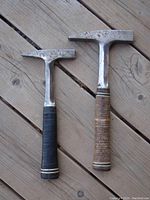 Two Estwing masonry/stone working hammers placed on wooden surface showing metal heads with pointed and flat sides and leather handles in black and tan color.