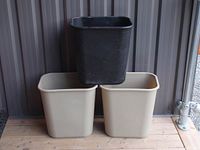 Photo of three Rubbermaid commercial garbage cans, two beige and one black, without lids, stacked with one black can on top of two beige cans.