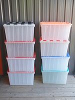 Eight transparent plastic storage bins stacked in two columns with color-coded lids, showing closed bins and the variety of lid colors.