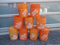 Photo showing the front view of all nine Home Depot buckets stacked in a pyramid shape outdoors, eight orange and one yellow bucket visible.