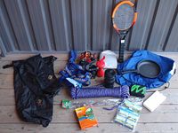 Lot of camping items including dry bags, rope, headlamps, frying pan, and insect repellents arranged on wood surface.