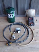 Photo showing green propane tank, adaptor hoses coiled with brass fittings and attached regulator, and portable heater.