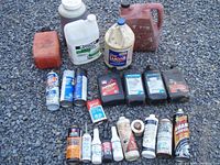 Full lot view showing multiple jugs, bottles, and sprays for car care on gravel ground.