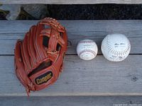 Full view of Cooper leather baseball glove with two balls (one baseball, one softball) on wooden surface.
