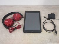 Red Sony wired headphones, black Dell tablet, and USB charger cable laid out on a table.