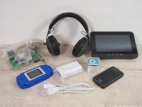 Full view of all electronics in the lot showing headphones, digital devices, cables, and circuit board