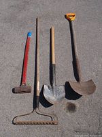 Full view of four garden tools laid out on the ground: sledge hammer, rake, rounded shovel, and square shovel