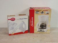 Photo showing original boxed Betty Crocker hand mixer and Sunbeam coffee maker side by side on table.