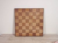 Front view of the square wooden chess/checkers board with alternating dark and light squares laid flat against a wall.