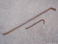 Two heavy duty pry bars on gravel surface, showing size difference and rusted condition