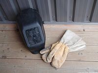 Light-colored leather welding gloves alongside the black Lincoln welding helmet on wooden surface.