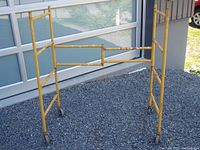 Yellow MetalTech folding scaffold frame standing upright on gravel with four attached castors.