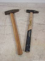 Top view of two wooden handled craft hammers with metal heads, one plain wood, one partially black painted with Peddiman label.