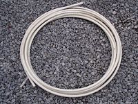 Full view of the coiled white PEX plumbing hose roll placed on gravel, showing the product form and size.