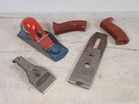 Stanley hand planer body, two blades, two wooden handles, and a blade baseplate on a flat surface.